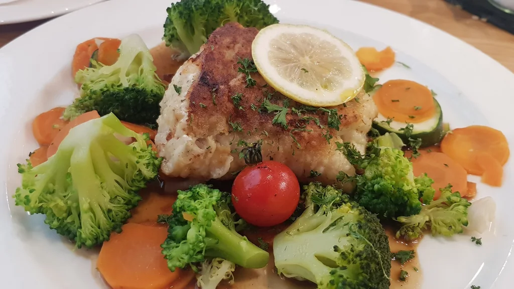 Filetto di pesce bianco rosolato servito su un piatto con verdure e una fetta di limone