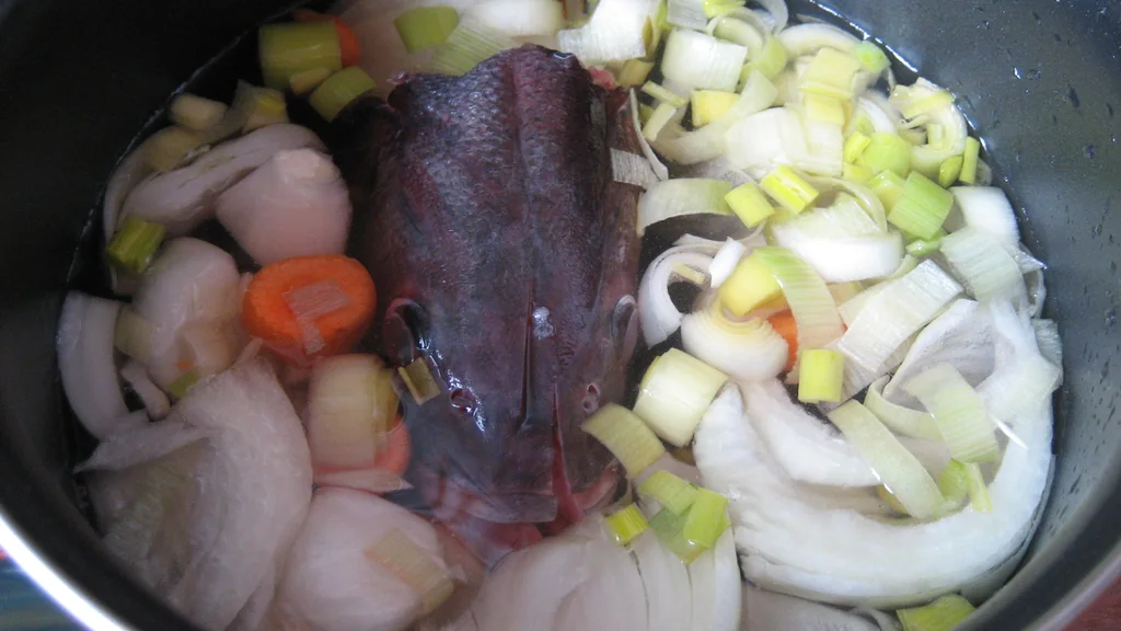 Preparazione di un fumet di pesce con testa di spigola e verdure aromatiche in pentola