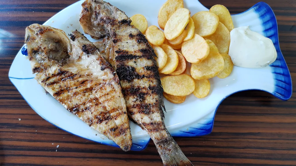 Dorade grigliata servita con patate fritte e salsa su un piatto a forma di pesce
